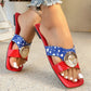 Close-up of red and blue color-blocked flat sandals with a large, ornate gold medallion buckle, worn by a person with white-painted toenails.