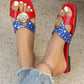 Zylpha flat slip-on sandals for women in vibrant red and blue color-block design, featuring a statement gold medallion buckle and white heart print on a blue strap. Shown with distressed denim jeans and an anklet.
