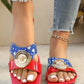 Zylpha bold statement flat sandals in vibrant red and blue with a gold medallion buckle, worn with distressed denim jeans and a gold anklet.