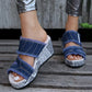 Zylva women's distressed denim wedge sandals with a striking newspaper print on the heel, featuring frayed edges and a silver buckle, worn with metallic trousers on a wooden deck.