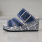 Side view of Zylva women's wedge sandals in blue denim with frayed edges and a silver buckle, featuring a black and white newspaper print on the wedge heel.