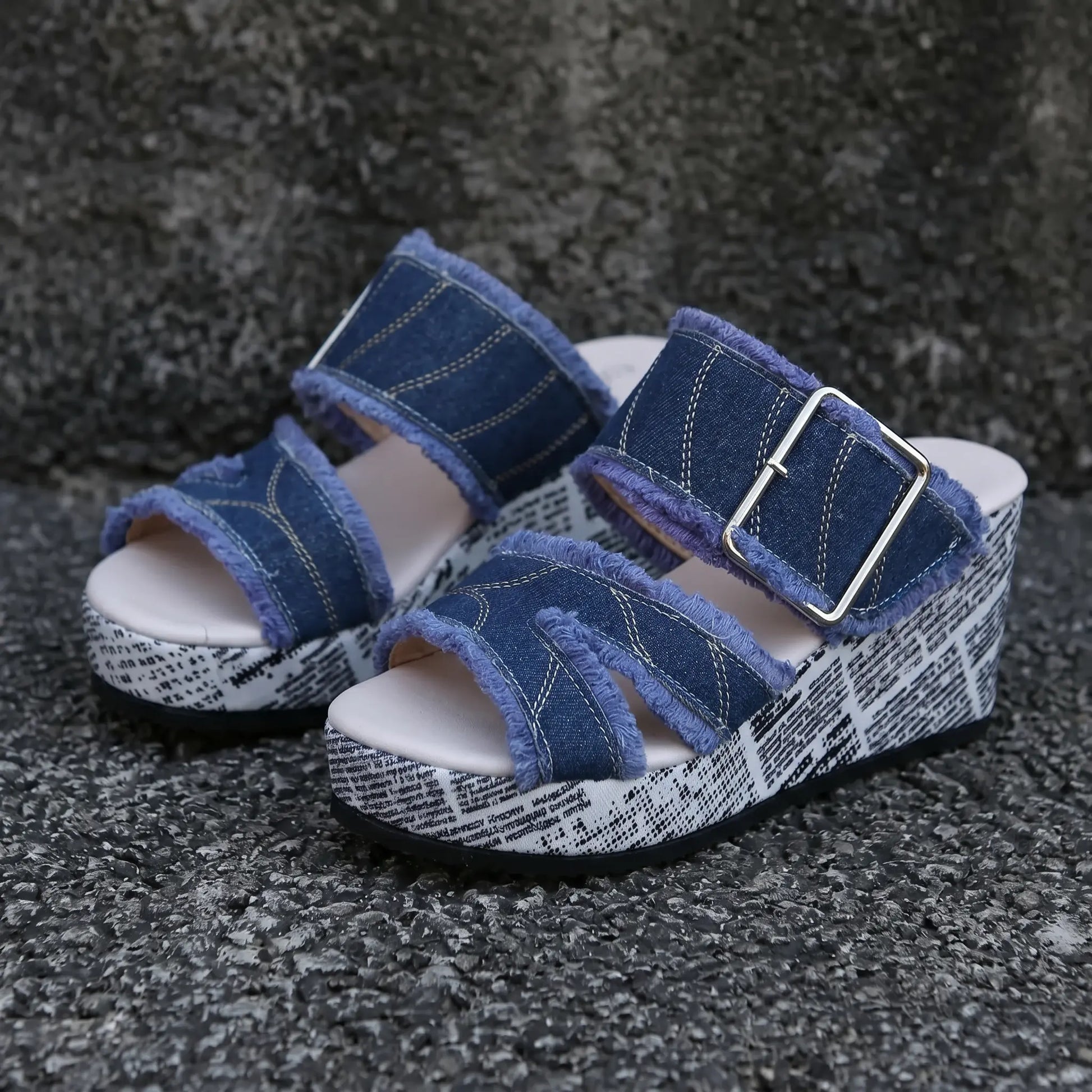 A pair of Zylva women's denim wedge sandals with frayed edges, a silver buckle, and a newspaper print on the wedge heel and platform.