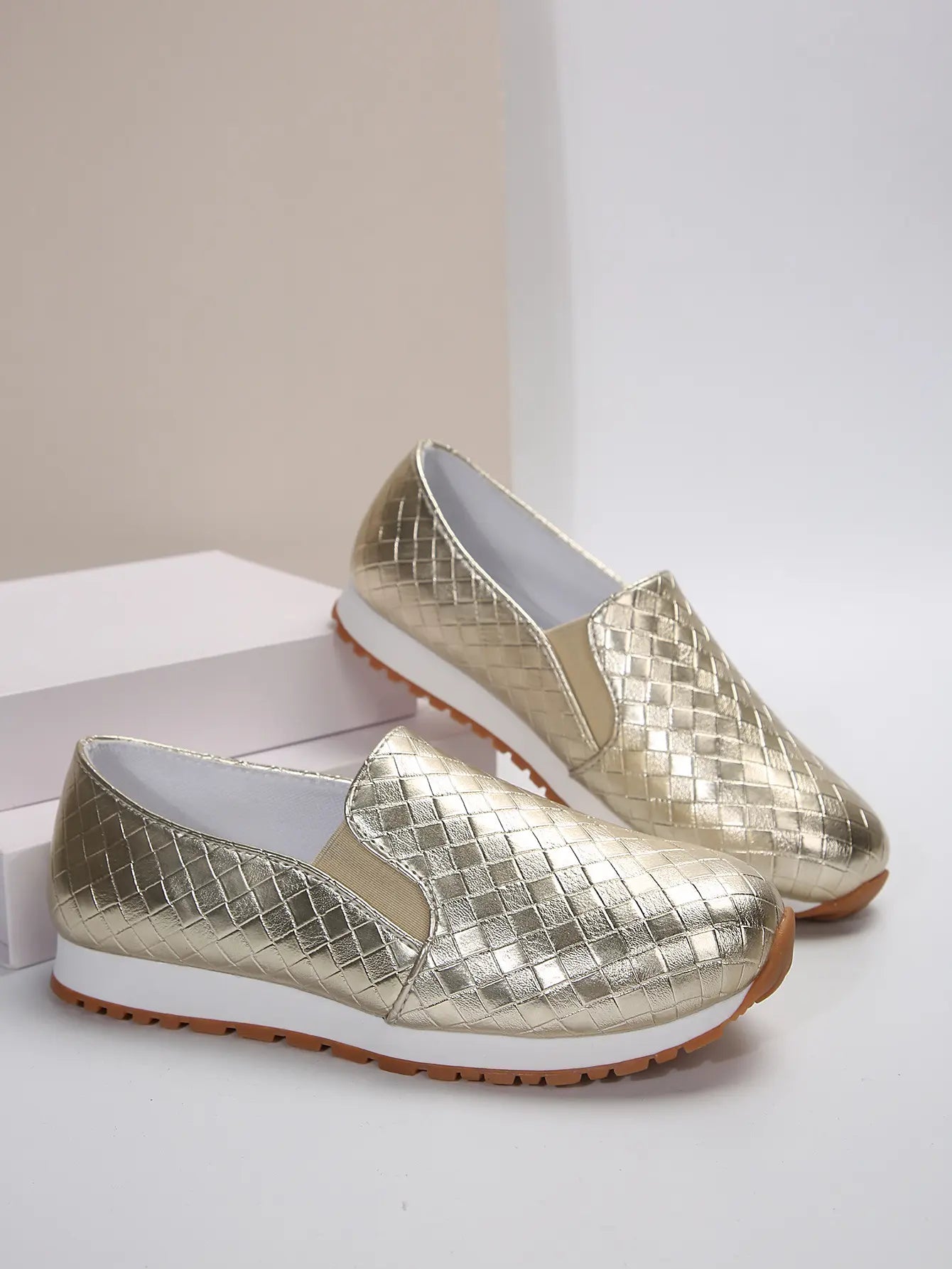 A pair of Zymir metallic gold slip-on loafers with a woven texture, displayed at a three-quarter angle on a studio background.