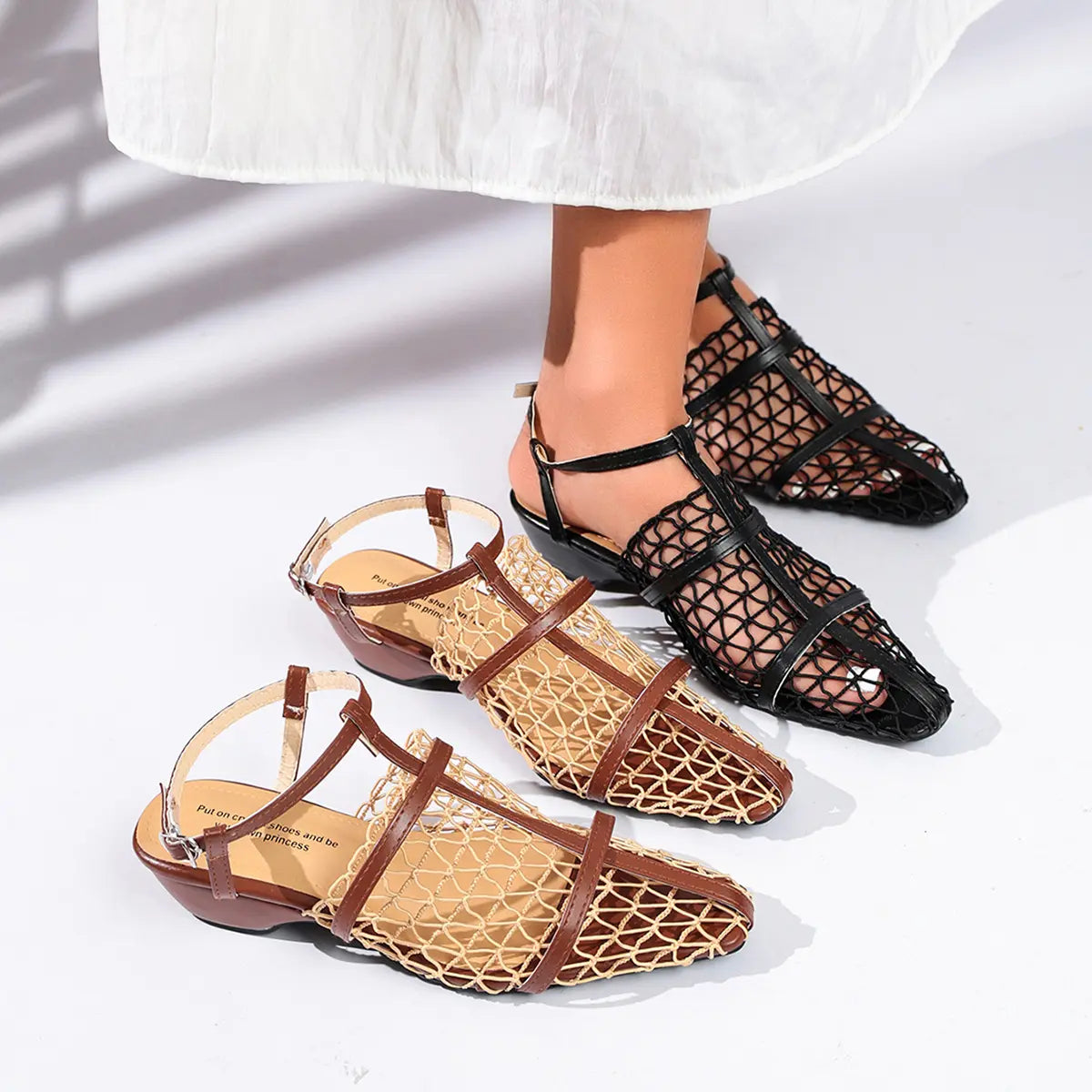 A pair of Zynthis black mesh heeled sandals with pointed toes and woven straps, worn by a model, shown alongside a brown woven variant on a clean white studio background.