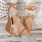 Shimmering metallic floral peep-toe wedge sandals in pale gold worn by a model with white-toe polish and a turquoise anklet, featuring elastic criss-cross straps with a gold-tone ring, set against a white-washed wood plank background.