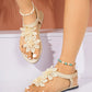 Close-up of Zyphir women's flat thong sandals in a light beige color, featuring delicate white lace floral embellishments on the vamp and a thin elasticated ankle strap. Shown on feet with white nail polish, styled on a clean studio background.