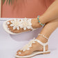 Off-white bohemian thong sandals adorned with delicate white lace floral embellishments and a thin elasticated ankle strap, shown on a model's feet with a summery background.