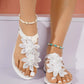 Close-up view of white Zyphir bohemian thong sandals adorned with delicate lace floral embellishments, worn on feet with starfish anklets.