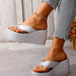 Women's shimmering silver metallic wedge platform flip-flops with a knotted toe strap and woven-textured wedge base, shown on feet with denim jeans.