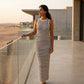Elegant woman in a Zyphron cream and navy striped ribbed knit maxi dress, showcasing the bodycon fit, on a modern balcony at sunset.