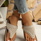 Woman's feet wearing beige laser-cut thong platform sandals with a cork-patterned footbed and gold buckle detail, paired with distressed denim jeans.