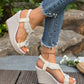 A woman's feet adorned with Zyra's cream off-white bohemian wedge sandals, featuring pearl and crystal embellishments on the T-strap and a textured linen-like wedge heel, styled with distressed denim.