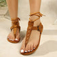Zyra bohemian flat sandals in deep brown suede-like material, featuring artisanal cross-stitching on the toe strap and braided ankle ties. The adjustable buckle strap offers a secure fit for a stylish, gladiator-inspired look.