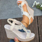 Close-up of an off-white bohemian wedge sandal adorned with faux pearls and iridescent crystals on a T-strap, worn on a foot against a natural wood and stone background. Features a textured woven wedge heel and peep-toe.